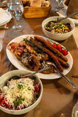 Meet plate on a restaurant table with sausages, meatballs, steak skewers, bacon, cherry tomatoes and salads