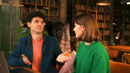 Expressive beautiful woman gesturing while talking with man sitting in modern cafe
