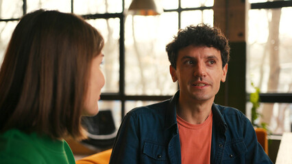 Expressive beautiful woman gesturing while talking with man sitting in modern cafe
