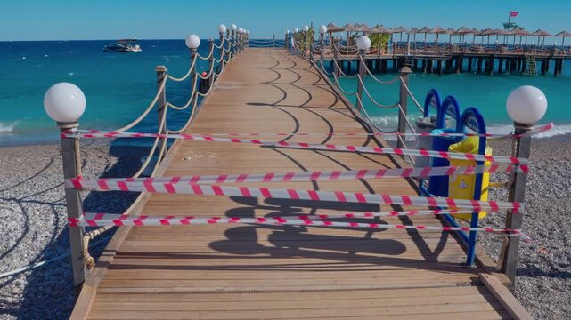 The pier is closed to vacationers due to rough seas and strong winds. Waves crash against the breakwaters, and the strips of the pier flutter and sway in the gusts of wind. The deserted shore and stor