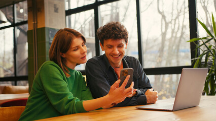 Couple, woman holding mobile phone using mobile app sitting in modern coworking