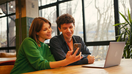 Couple, woman holding mobile phone using mobile app sitting in modern coworking