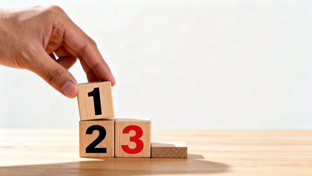 Hand placing wooden block with number one on top of blocks numbered two and three, forming a stepped arrangement on a wooden surface. - Powered by Adobe
