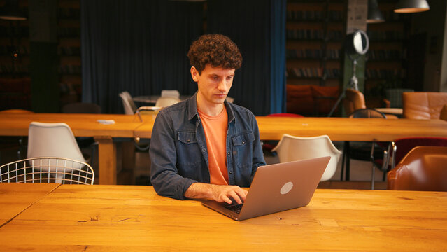 Focused male student working on laptop in university library or in modern coworking