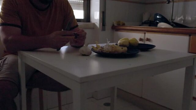 Man peeling fresh garlic cloves in kitchen