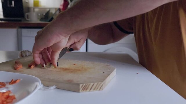 Person preparing food slicing garlic on a wooden cutting board
