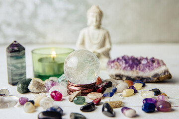 Various semi precious stones scattered, gemstone crystal sphere or crystal ball and white sitting Buddha. Spiritual background concept.