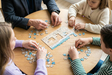 High angle view of a multigenerational family working together to solve a jigsaw puzzle on a round wooden table at home, focusing on teamwork and leisure