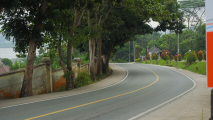 Fototapeta premium Curving Rural Road Surrounded by Trees and Lush Greenery