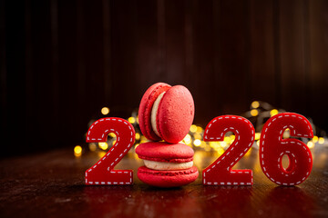 New year 2026 composed with red felt numbers and a stack of delicious red macarons, symbolizing sweet celebrations and holiday concepts on a dark wooden background with bokeh lights