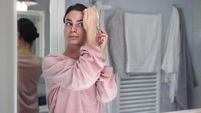A young woman looking at her face in the mirror in the bathroom. Concept self-reflection.