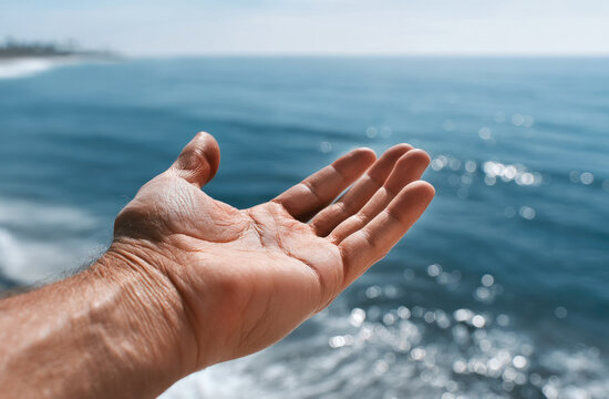 Outstretched hand reaching toward blue ocean horizon, sunlight reflecting on water, peaceful and inviting summer scene - Powered by Adobe