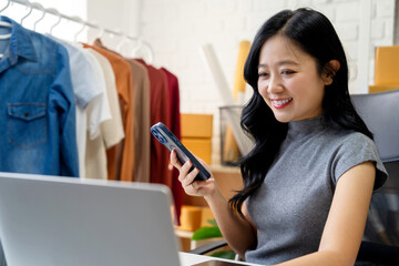 SME Startup, Small Business Entrepreneur. Happy beautiful smiling Asian businesswoman holding a mobile phone while working at home.