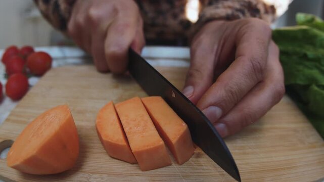 Preparing a vegetarian dinner. A man slices a peeled sweet potato on a wooden cutting board. Healthy eating. Close-up.