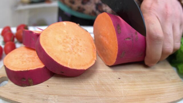 A man slices an unpeeled sweet potato on a wooden cutting board. Preparing a vegetarian dinner. Healthy eating. Close-up.