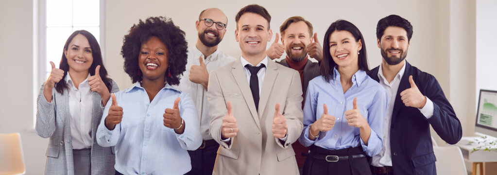 Group portrait of a multinational business team showing thumbs up in an office. People positive attitude and success, highlighting teamwork and collaboration in achieving business goals.