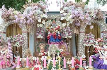 Statue of Sri Maha Lakshmi Devi or Ambabai is a Hindu goddess of wealth, prosperity and fortune with Other gods on a decorated platform with candles and an elaborate pink and white floral arrangement.