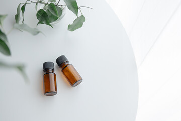 Two amber essential oil bottles on white table with green plant, minimal natural light