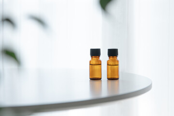 Two amber essential oil bottles on white table with soft greenery, horizontal copy space