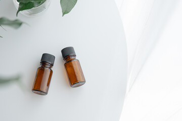 Two amber essential oil bottles on white table with green plant, minimal natural light