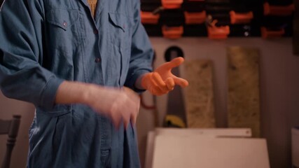 Close-up of carpenter or repairman in uniform standing at workshop and putting gloves preparing for work. mechanic putting glove
