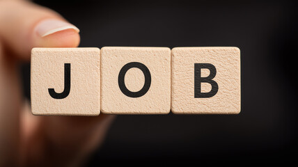 A hand holding wooden blocks forming the word job symbolizing personal agency responsibility and the active pursuit of professional opportunities.
