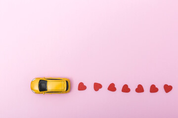 Yellow toy car on a pink background, leaving a trail of red heart shapes, symbolizing love and affection in a playful and creative way, perfect for romantic themes