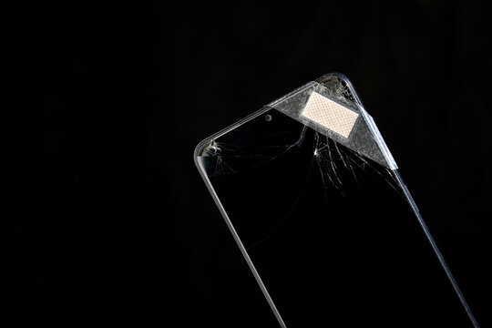 Smart Phone com display quebrado com um curativo aplicado, em auto contraste num fundo preto