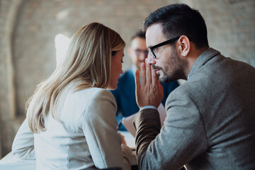 Two businesspeople whisper secretly to each other in the foreground, while a worried client stands...
