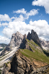Dramatic view of the Odle peaks from Seceda in Val Gardena, Dolomites. Sharp limestone spires rise above green alpine ridges under bright blue sky with clouds an iconic landscape of the Italian Alps