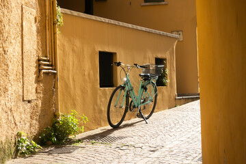 Light blue bike standing parked on its stand by a yellow ochre plaster stone wall on a sunny street in an old Italian town