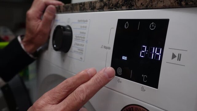 Close-up of a man's hands setting the washing machine's functions, adjusting the program, temperature, and spin cycle on a modern appliance