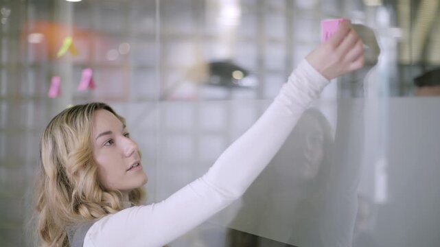 Young businesswoman brainstorming ideas with sticky notes on a glass wall