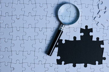 Problem solving concept. an incomplete puzzle with magnifying glass revealing black background copy...