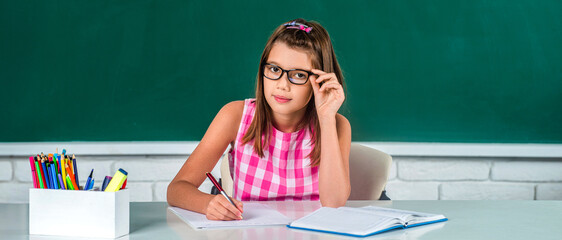 Happy cheerful smiling cute schoolgirl with in classroom on chalkboard blackboard background