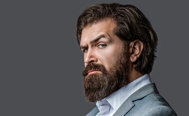 Closeup portrait of handsome businessman in formalwear suit. Portrait of confident businessman man, suit with beard and hair alone looking seriously and confidently at the camera on gray background