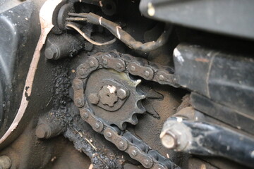 View of bike engine output shaft that is connected to the rear wheel with the help of gear and chain system. Greasy and rusty engine parts
