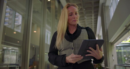 Woman examining tablet with serious focused expression in hallway, standing still while checking digital content, working or preparing for task