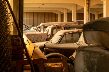 Sunlit warehouse of dusty vintage cars - rusty classic vehicles and barn-find autos in an abandoned...