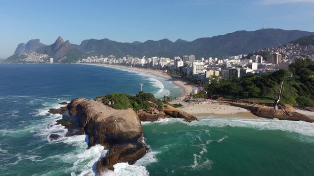 Aerial drone shot flying over Pedra do Arpoador toward Ipanema Beach on a sunny day in Rio de Janeiro, Brazil.	
