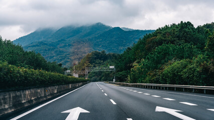 Fototapeta premium Scenic highway with arrows leading through lush greenery and mountains