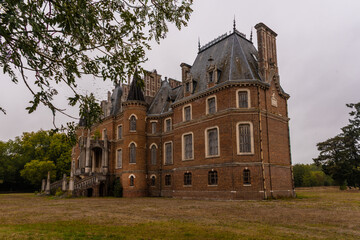 Empty French château with turrets and mansard roof - weathered brick manor in overcast countryside © Carismarkus