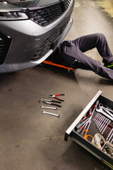Mechanic lying underneath a raised vehicle in the workshop. Repair, inspection, and maintenance of the car underbody.