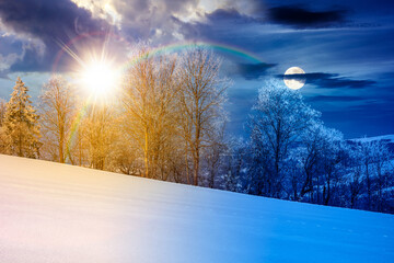 trees in hoarfrost on snow covered meadow. day and night time change concept. beautiful mountainous countryside landscape with sun and moon. cold winter atmosphere. harmony and progress calendar