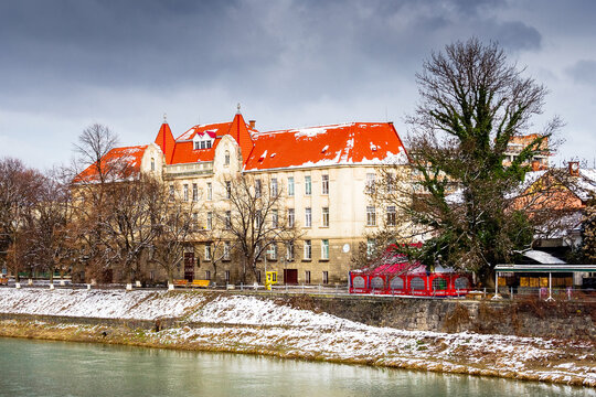 uzhhorod, ukraine - 15 feb 2009: uzh river in the old city in winter. cityscape with snow on the embankment. european urban landscape with school building. dramatic weather with cloudy sky