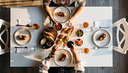 Overhead view of a delicious brunch table setting, featuring various food and drinks with people enjoying their meal.