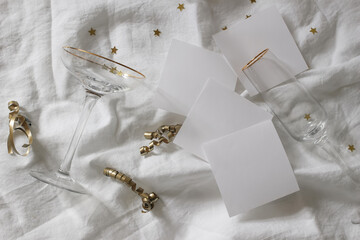 Champagne glasses. Golden star confetti tinsel on white linen table cloth background. Celebrate, birthday party concept. New Years flatlay, top view. Blank paper card mockups. Festive holiday banner