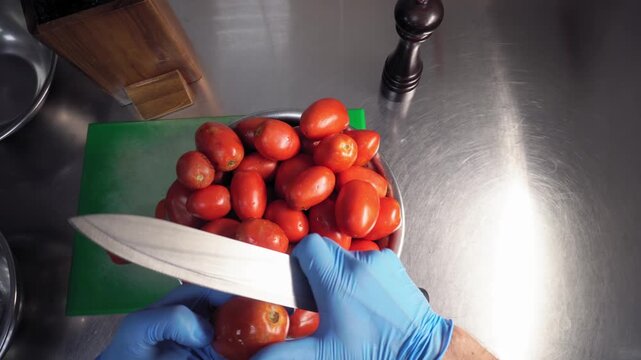 The cook takes a tomato from the bowl, examines it, and cuts off unusable parts