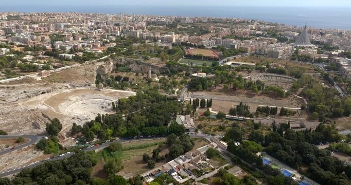 Aerial view of the Neapolis Archaeological Park, located in Syracuse, Sicily, Italy. In the background, at horizon, there's the modern city overlooking the Mediterranean Sea. Sunny summer morning.