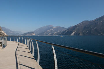 Obraz premium Panoramic view of the Limone sul Garda cycle path stretching above the lake, with sweeping curves, blue water, and dramatic cliffs creating one of the most scenic routes on Lake Garda.